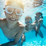 Article thumbnail: Happy kids having underwater party in the swimming pool. The boy is grinning at the camera. Shot with Nikon D850.