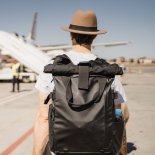 Article thumbnail: white young man with hat and suitcase walking through the airport near the takeoff runway